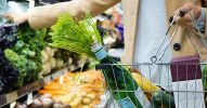 Person in einem Supermarkt, die einen Korb mit frischen Lebensmitteln hält.