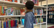 Kleines Kind steht in einer Bibliothek vor dem Bücherregal